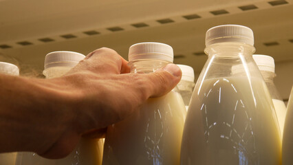Close-up of many plastic milk bottles on the fridge shelf and a male buyer takes one