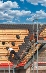 Bauarbeiten / Dachdeckerarbeiten: Dachdecker deckt Steildach eines eingerüsteten Neubaus / Rohbaus...
