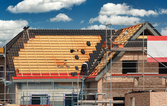 Bauarbeiten / Dachdeckerarbeiten: Dachdecker deckt Steildach eines einger&uuml;steten Neubaus / Rohbaus ein