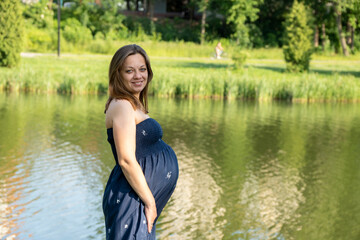 Pretty pregnant woman relaxing near the pond on the meadow in the park. Happy parenthood, healthy pregnancy. Happy pregnancy concept