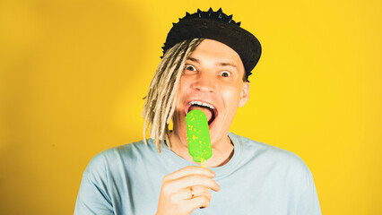 Young funny man in black cap licking ice cream. Excited male with bizarre facial expression eating...