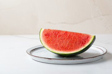 Slice of red watermelon on a plate on light surface copy space