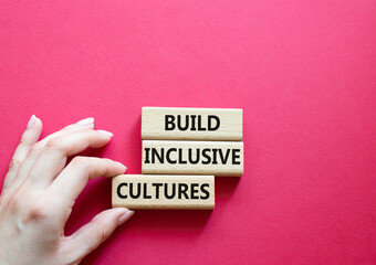 Build Inclusive Cultures symbol. Wooden blocks with words Build Inclusive Cultures. Beautiful red background. Businessman hand. Business and Build Inclusive Cultures. Copy space.