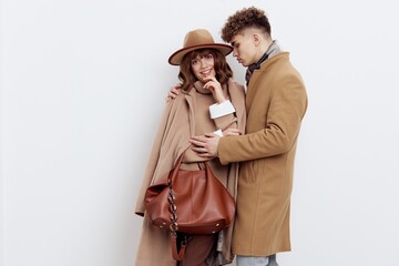 a cute couple in love a man and a woman in a stylish autumn rain stand hugging on a white background and a woman holds a brown bag in her hand