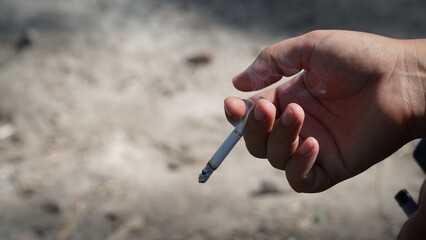 A hand holds a smoking cigarette on a dark background copy space. harm from cigarette smoking. Smoker.