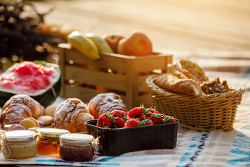 summer picnic basket with fruit and bakery on a blanket outdoors. Lunch with croissants, jam, watermelon, strawberry and fresh fruits in wooden box in the park. Copy space.
