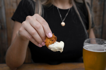 Eating seafood at the restaurant. Closeup view of a woman's hand, holding a fried shrimp dipped in...