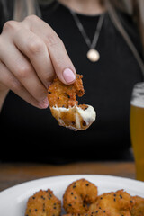 Seafood. Closeup view of a woman's hand, holding a fried shrimp dipped in aioli and teriyaki sauce A pint of beer besides the dish.