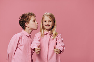 cute, beautiful children are standing in pink clothes on a pink background and the boy reaches out to kiss the girl on the cheek. The topic of relationships