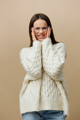 An emotional, loudly screaming woman stands on a beige studio background in a white sweater with her eyes closed