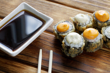 Crispy tempura - rolls with rice, nori, fish and sauce next to the Japanese gravy boat - seyuzaru with chopsticks - varibashi. Table made of natural pine boards. Macro. Selective focus.
