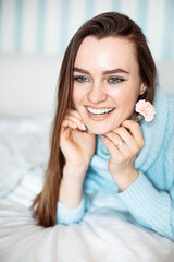 Smiling happy woman lying on bed in cozy sweater, holding delicate flower in hand, closeup portrait 