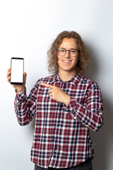 Handsome young man holding smartphone with white blank screen. The guy points his finger at the blank mobile phone mockup.