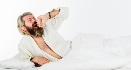 Handsome bearded man in morning yawning and stretching in bed. Sleepy guy in bathrobe. Awaking.