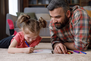 Young handsome father and cute daughter playing together. Dad and child are painting picture lying...