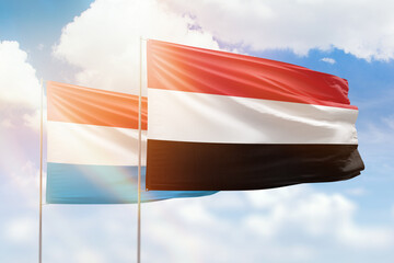 Sunny blue sky and flags of yemen and luxembourg