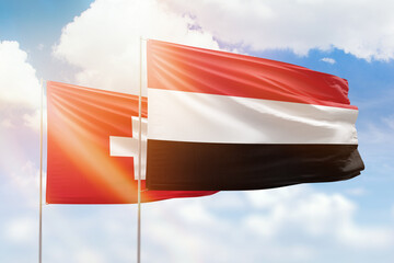 Sunny blue sky and flags of yemen and switzerland