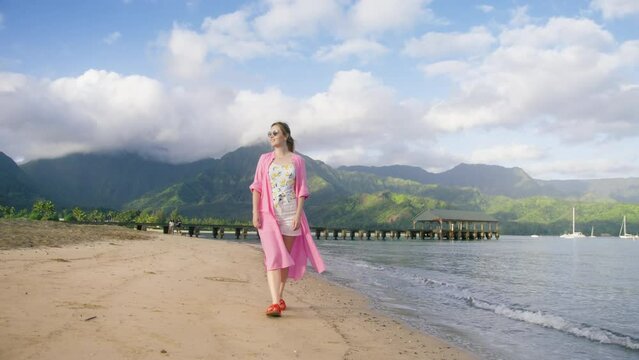 Free woman on morning walk by empty sandy beach on tropical Hawaii island with cinematic high green mountain on background. Summer vacation dream concept. Happy free traveler enjoying outdoor trip USA