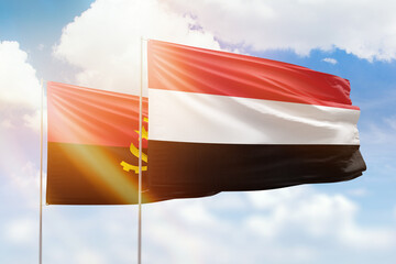 Sunny blue sky and flags of yemen and angola