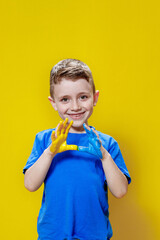 Little happy boy with painted palms in yellow and blue, the colors of the flag of Ukraine. Ukrainian creative preschooler
