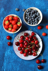 Summer still life with fresh berries on ceramic plates. Top view photo of organic cherry, blueberry and strawberry. Healthy eating concept. 