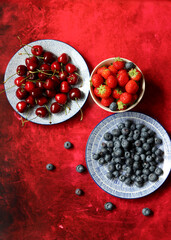 Summer still life with fresh berries on ceramic plates. Top view photo of organic cherry, blueberry and strawberry. Healthy eating concept. 