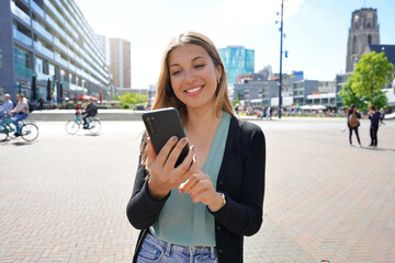 Portrait of multi ethnic young woman using smartphone app in Rotterdam modern city square,...