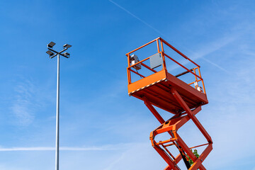 Orang lifting tower climbs up to a street lamp.