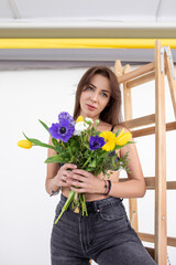 Bouquet of spring flowers. Beautiful young woman with dreamy look holds flowers in her hands, standing in studio . 