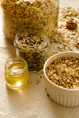 White bowl with nuts, jars with muesli, honey and seeds, ingredients for granola 