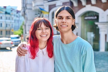 Happy couple of teenage friends hugging looking at camera, on city street