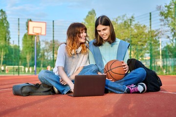 Friends students sitting on school basketball court looking at laptop