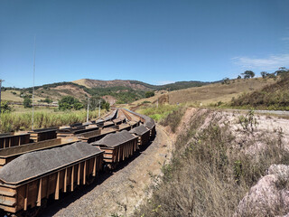 Rural landscape showing clear blue sky, hills, mountains, full and empty train cars at Itabira Minas Gerais, Brazil