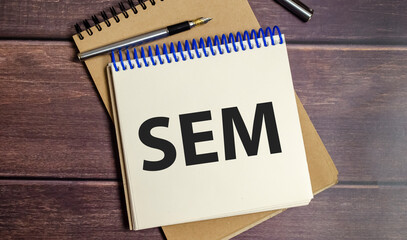 notebook with the word SEM Search Engine Marketing on wooden background