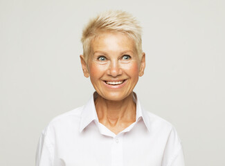 Life only starts when get older. Portrait of happy and charming european senior woman with blond short hair over grey background.