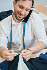Cheerful male dressmaker talking on smartphone in workshop