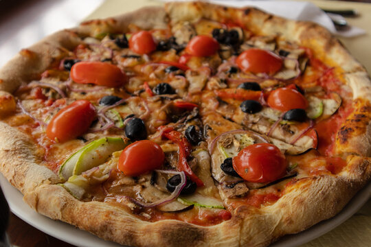 photography of a vegetarian pizza with fresh vegetables (tomatoes, olive, pepper, zucchini, onion)