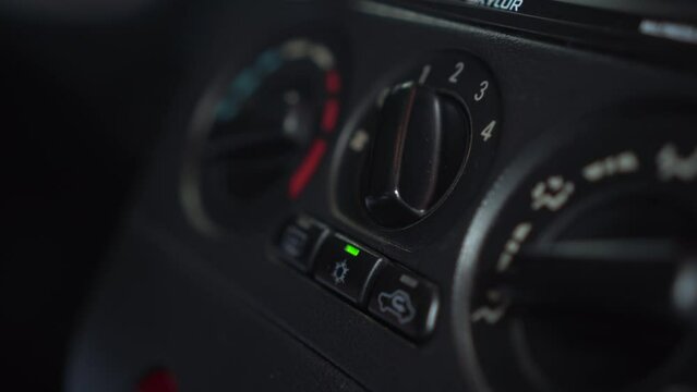 The woman turns on the fan and presses the air conditioner button in the car. Automotive panel close-up.