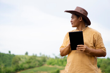 Asian man botanist wears hat, holds smart tablet, stand at nature forest. Concept : Nature survey, use wireless technology and internet to manager environment.