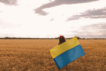 Young pretty girl holds flag and waiting for victory in the field wearing Ukrainian national...