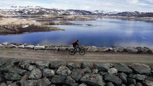 Aerial Follow Shot Of Male Cycling Across Sysen Dam In The Municipality Of Eidfjord in Hordaland, Norway. Tracking Shot