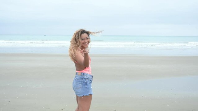 Curly latina walking over the beach and waving "come here".
