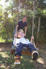 Dad Pushing Son on Swing in a Sunny Day. Family Time with a Father and Son Playing Together.