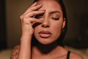 Emotional portrait of a beautiful Latin girl cover her face with hand indoors.