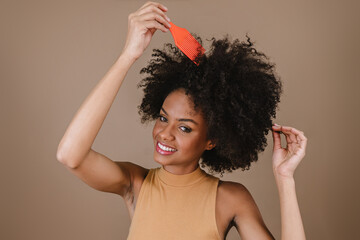 Young Latin woman combing hair. Fork for combing curled hair. Pastel background.