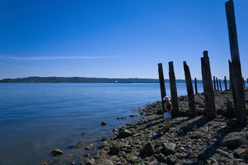 A woman wearing white shorts, a tank top, sunglasses, and a summer hat looking out over Puget Sound on a sunny day in Tacoma, Washington.