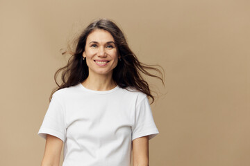 Obraz premium portrait of a beautiful attractive woman with long, beautiful, well-groomed hair blowing in the wind, stands smiling cutely at the camera on a beige background.