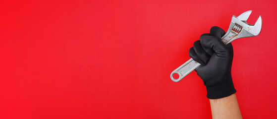 hand wearing black gloves holding silver spanner wrench isolated on wide red background