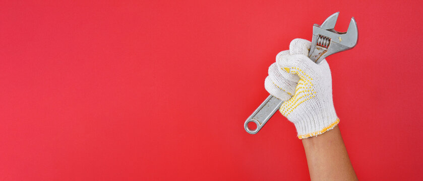 hand wearing white gloves holding silver spanner wrench isolated on wide red background