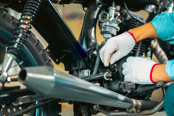 Choseup man mechanic in garage or workshop inspecting classic motorcycle during the maintenance and checks oil level.